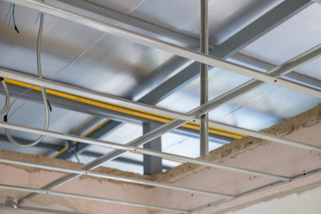 An interior renovation project focuses on ceiling framework installation. exposed electrical wiring runs along new aluminium grid system before final finishingの写真素材
