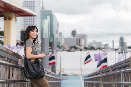 A happy young southeast asian woman, travel blogger searching map on smartphone. tourism explorer guide for local cultural experience in bangkok thailand near chao phraya riverの写真素材