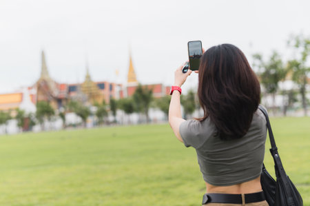 A happy southeast asian teenager woman solo world travel explorer and blogger use smartphone to take photo for local cultural experience tourism concept in bangkok thailand and asiaの写真素材