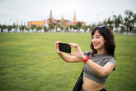 A happy southeast asian woman teenager blogger explorer on solo world travel take photo with smartphone for local cultural tourism experience concept in bangkok thailand asiaの写真素材
