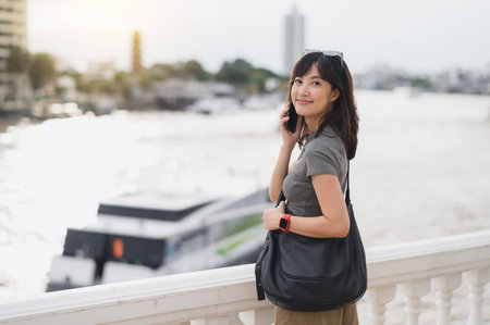 A happy southeast asian teenager solo world travel explorer blogger on tourism trip in asia. local cultural experience in bangkok thailand wait for an express boat on chao phraya riverの写真素材