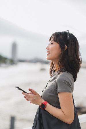 A happy young southeast asian woman, teenager blogger searching map smartphone, tourism guide. world travel explorer local cultural experience concept chao phraya river, bangkok, thailand, asiaの写真素材