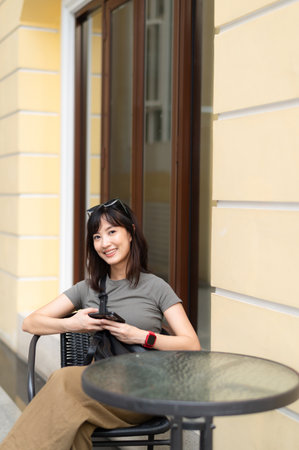 A young southeast asian woman in 30s like teenager blogger working outside coffee shop room with old architecture searching internet on smartphone feeling happyの写真素材