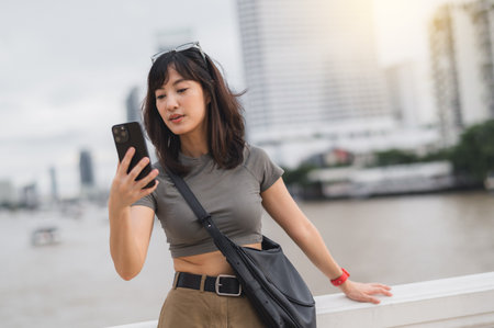 A young southeast asian woman teenager blogger using smartphone searching for guide. world travel explorer by chao phraya river in bangkok. asia tourism concept local cultural experienceの写真素材