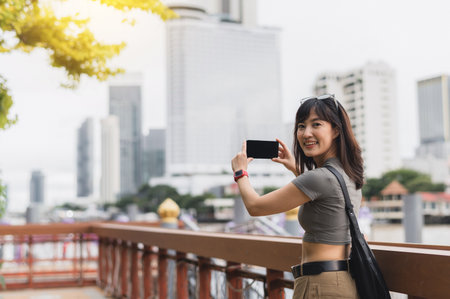 Happy solo southeast asian woman and teenager blogger take photo with smartphone. world travel explorer having local cultural experience for tourism Bangkok Thailand wait for an express boat Chaoの写真素材