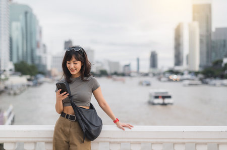 Happy young southeast asian woman teenager blogger and world travel explorer using smartphone searching tourism guide Chao Phraya river Bangkok Asia. local cultural experience tourism conceptの写真素材