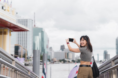Happy solo Southeast Asian woman teenager blogger world travel Bangkok Thailand. smiling explorer take photo with smartphone to express local cultural tourism experience and concept Chao Phrayaの写真素材