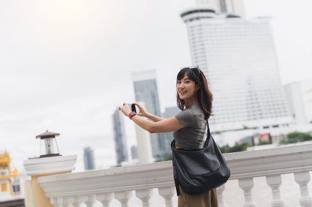 Happy solo southeast asian woman travel blogger take photo with smartphone. world tourism concept and local cultural experience for an explorer on Chao Phraya River in Bangkok Thailandの写真素材