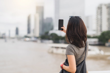 Solo southeast asian woman teenager blogger world travel explorer take photo with smartphone. Express local cultural experience wait for boat chao phraya river bangkok thailand. Asia tourismの写真素材