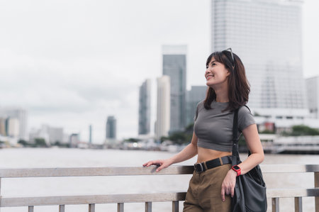 Happy solo Southeast Asian woman teenager blogger world travel tourism. An explorer enjoys local cultural experience Bangkok Thailand. Wait for express boat Chao Phraya River. travel concept Asiaの写真素材