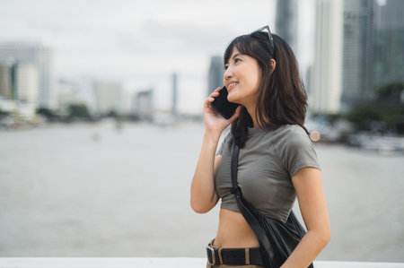 Solo Southeast Asian woman teenager blogger enjoy world travel tourism Bangkok Thailand. happy explorer express to friend via smartphone local cultural experience and wait for boat Chao Phrayaの写真素材