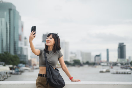 Beautiful young southeast asian woman blogger in 30s taking selfie with smartphone. World travel explorer local cultural experience summer tourism concept at Chao Phraya River Bangkok Asiaの写真素材