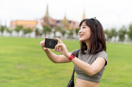 Happy southeast asian woman teenager blogger on solo travel in Bangkok Thailand take photo with smartphone. world explorer concept for asia tourism and local cultural experienceの写真素材