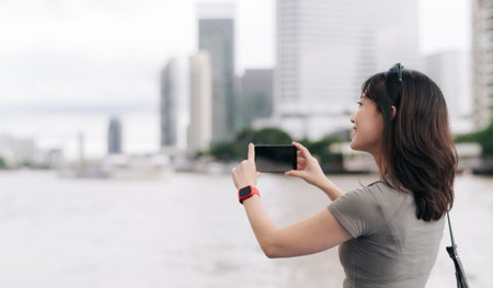 Solo southeast asian woman teenager blogger world travel explorer take photo with smartphone express boat. Local cultural experience for asia tourism concept. Wait Chao Phraya River Bangkokの写真素材