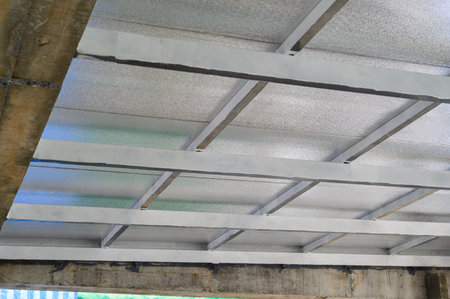 Grey metal sheet panels compose an overhead structure featuring sturdy supports and insulation. Industrial materials like pu foam provide sense of safety and durability for ceiling coveringの写真素材