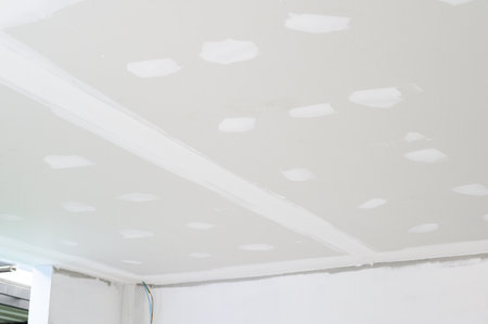 Smooth plastering applied to gypsum board ceiling during interior renovation building project. Essential edges finishing before electrical wire installation on ceilings continues constructionの写真素材