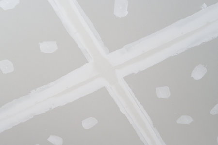 Gypsum board ceiling undergoing interior building renovation smooth plastering on edges. Preparation work for ceilings finishes surface. Electrical wire pathways become hidden during applicationの写真素材