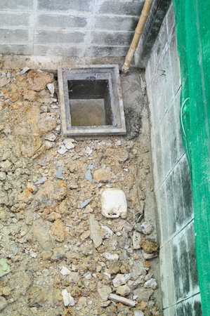 Dirty ground at construction site showing plumbing drain pit during house renovation project. concrete floor repair reveals messy unfinished work on systemの写真素材