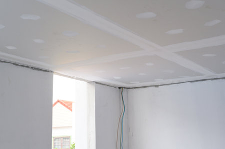 Interior renovation project building gypsum board ceiling plastering smooth edges with electrical wire installation detail. Ceiling construction progresses towards achieving smooth finishの写真素材