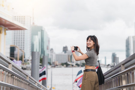Solo Southeast Asian woman teenager travel blogger and world explorer take photo with smartphone by Chao Phraya river Bangkok Thailand. Asia tourism local cultural experience conceptの写真素材