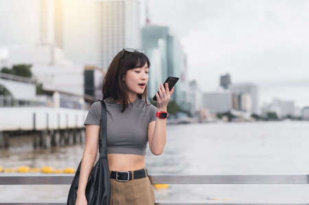 Happy southeast asian woman teenager blogger solo travel Bangkok Thailand. local cultural tourism experience using smartphone to express message and wait for friend or boat Chao Phraya riverの写真素材