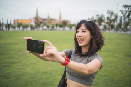 Happy southeast asian woman teenager blogger on solo world travel take photo with smartphone. Local cultural experience for asia explorer tourism concept in Bangkok Thailandの写真素材