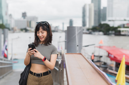 Young southeast asian woman teenager blogger and world travel explorer using smartphone searching tourism guide for local cultural experience concept in Bangkok Asia by Chao Phraya Riverの写真素材