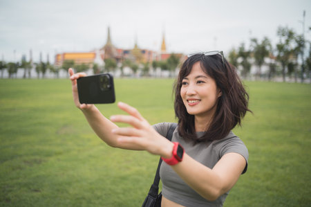 Happy southeast asian woman teenager blogger on solo world travel in Bangkok Thailand take photo with smartphone for local cultural tourism experience concept in Asia for an explorerの写真素材