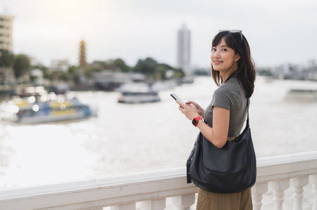 Young southeast asian woman teenager blogger world travel explorer searching smartphone map guide for local cultural experience. Asia tourism concept in Bangkok Thailand by Chao Phraya riverの写真素材