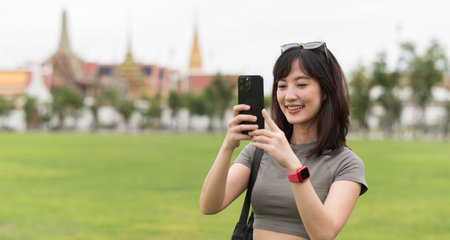 Happy solo Southeast Asian woman teenager blogger and world travel explorer enjoying tourism concept in Asia use smartphone to take photo for local cultural experience in Bangkok Thailandの写真素材