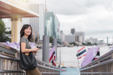 Happy young southeast asian woman travel blogger searching on smartphone map. World explorer enjoying local cultural experience and tourism in Bangkok Thailand by Chao Phraya Riverの写真素材