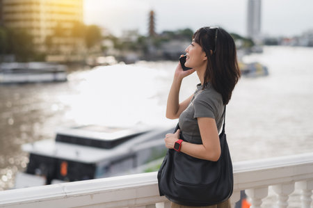 Content solo southeast asian woman teenager blogger on travel tourism in Bangkok Thailand. An explorer wait for local boat on Chao Phraya river in Asia using smartphoneの写真素材