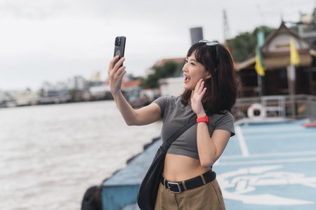 Happy solo southeast asian woman teenager blogger boat. World travel explorer local cultural experience. Asia tourism concept to express joy to friend smartphone and wait Chao Phraya River Bangkokの写真素材