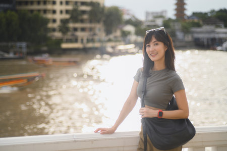 Happy young solo southeast asian woman blogger on world travel tourism. Explorer with smartphone enjoys local cultural experience by Chao Phraya River in Bangkok, Thailand. Asia conceptの写真素材