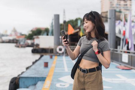 Solo southeast asian woman teenager blogger world travel explorer happy with smartphone. Wait for friend express boat Chao Phraya River Bangkok Thailand. Local cultural asia tourism experienceの写真素材