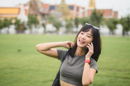 Happy southeast asian woman teenager blogger on solo world travel explorer tourism in Bangkok, Thailand. concept for local cultural experience in Asia, using smartphone to take photoの写真素材