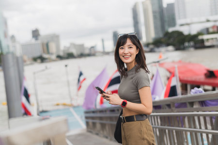Smiling young southeast asian woman teenager blogger world travel explorer using smartphone searching tourism guide. Local cultural experience concept in Asia by Chao Phraya River Bangkokの写真素材