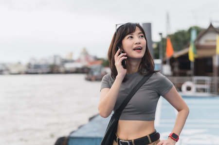 Solo Southeast Asian woman teenager blogger on world travel tourism express surprise. Wait for friend local boat cultural experience concept smartphone at Chao Phraya River Bangkok Thailand Asiaの写真素材