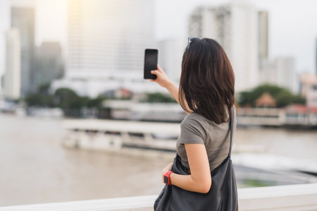 Happy solo southeast asian woman blogger and teenager take photo with smartphone. world travel explorer local cultural experience tourism concept Asia. Wait for express boat Chao Phraya riverの写真素材