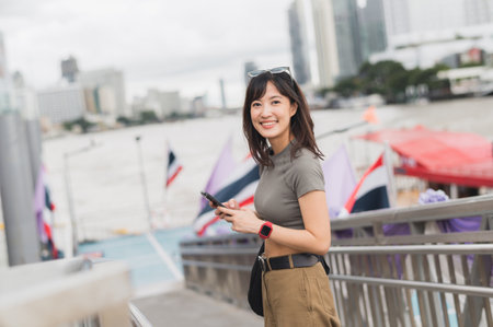 Young southeast asian woman teenager blogger using smartphone searching for travel guide. world explorer on local cultural experience near Chao Phraya river Bangkok. Asia tourism conceptの写真素材