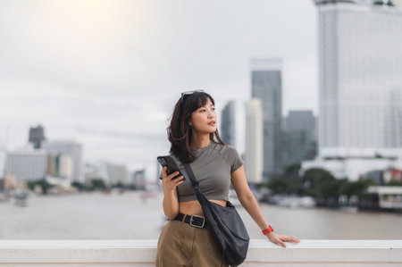 Young southeast asian woman teenager blogger and world travel explorer using smartphone searching tourism guide, having local cultural experience by Chao Phraya river Bangkok. Asia world travelの写真素材