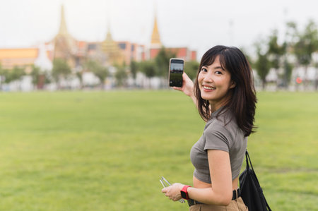 Happy southeast asian woman teenager blogger on solo world travel. An explorer local cultural tourism experience in Bangkok Thailand. Take photo with smartphone. Asia travel conceptの写真素材