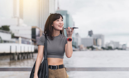 Happy solo southeast asian woman teenager blogger on travel tourism trip. Local experience in Bangkok Thailand. Wait for friend express joy with smartphone near boat on Chao Phraya river in Asiaの写真素材