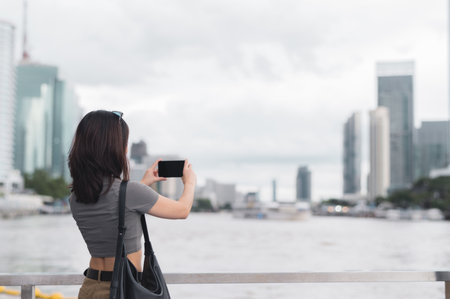 Solo southeast asian woman teenager blogger world travel explorer take photo with smartphone on express boat. Local cultural experience asia tourism concept on Chao Phraya River Bangkok Thailandの写真素材