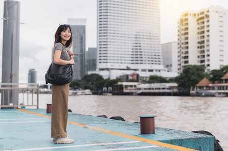 Happy southeast asian woman teenager blogger express joy during solo world travel tourism Bangkok Thailand wait for boat Chao Phraya river local cultural experience concept for explorer Asiaの写真素材