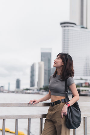 Solo Southeast Asian woman teenager blogger and world travel explorer waits for boat on Chao Phraya river. Happy express tourism concept for local cultural experience in Bangkok, Thailand, Asiaの写真素材