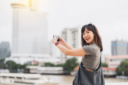 Happy solo southeast asian teenager woman blogger take photo with smartphone. World travel tourism concept, express boat on Chao Phraya River Bangkok Thailand. local cultural asia experienceの写真素材