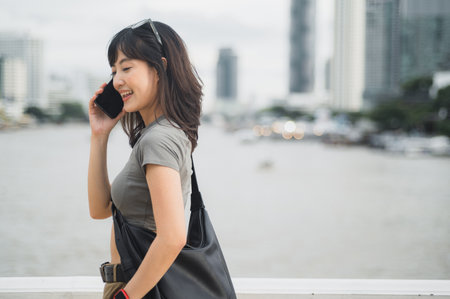 Happy solo Southeast Asian woman teenager blogger express joy with smartphone. World travel explorer local cultural experience. Tourism concept wait for friend boat Chao Phraya river Bangkokの写真素材