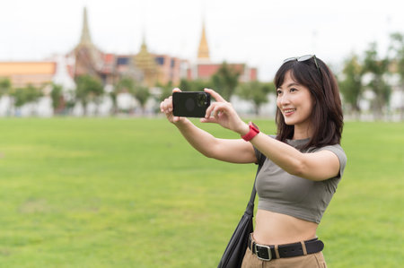 Happy southeast asian woman teenager blogger on solo world travel use smartphone to take photo....
