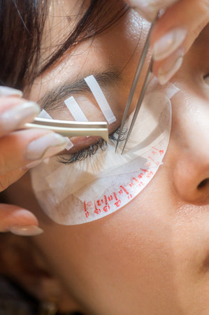 Relaxed young southeast asian woman during an eyelashes extension procedure in beauty salon. female...